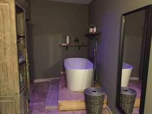 Une salle de bain avec une baignoire, un miroir, une étagère contenant des articles de toilette et un meuble en bois.