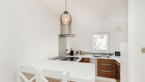A modern kitchen with white cabinetry, a stainless steel range hood, and a white dining table with chairs. - Welcoming 1BR flat near Park (Edinburgh)