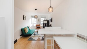 A modern living room with a green sofa, a small table, and a chair. There is a kitchen area with a white countertop and a hanging light fixture. - Welcoming 1BR flat near Park (Edinburgh)