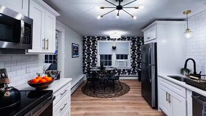 A modern kitchen with white cabinetry, a black and white patterned backsplash, a central island with a round table, and a stainless steel refrigerator.