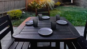 An outdoor dining table with plates and cups, surrounded by a wooden fence and string lights.