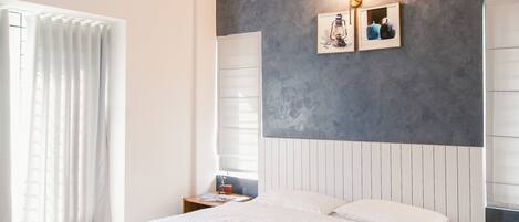 Een slaapkamer met een groot bed, een plafondventilator, een airconditioningapparaat, een nachtkastje en een wandlamp.