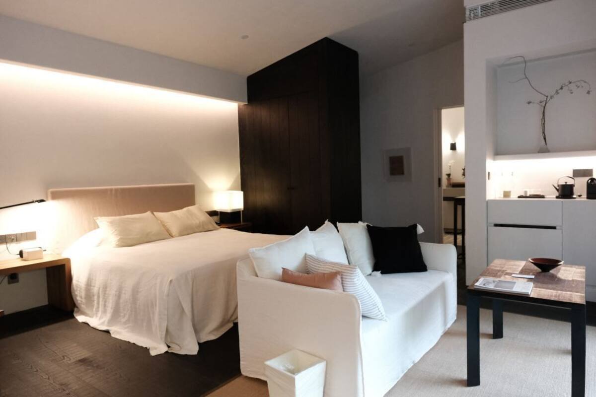 A modern hotel room with a large bed, a white sofa, a small table, and a wall-mounted artwork.