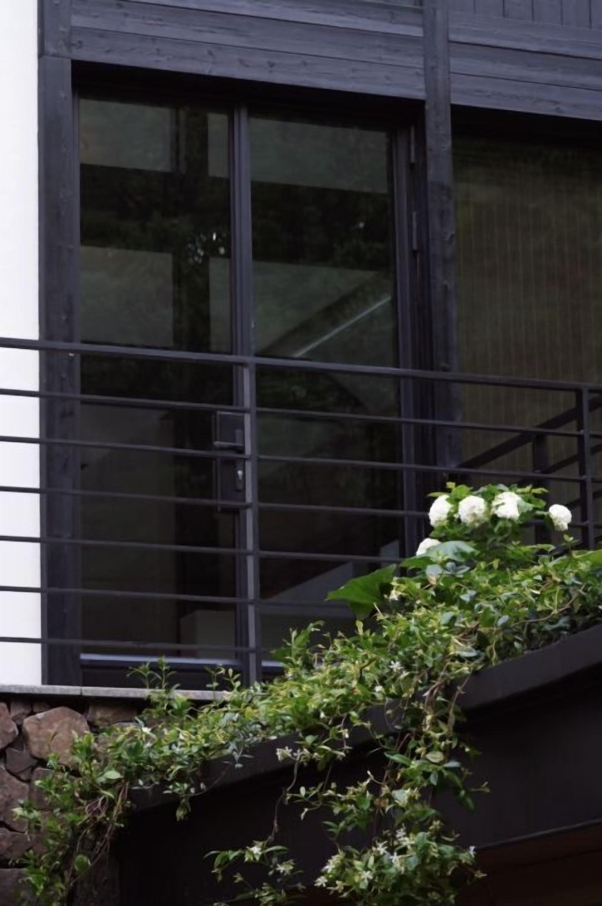 A building facade with large windows, a stone wall, and a climbing plant with white flowers.