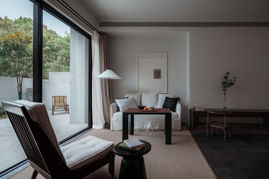 A modern, minimalist living room with a large window, a sofa, a coffee table, and a side table.