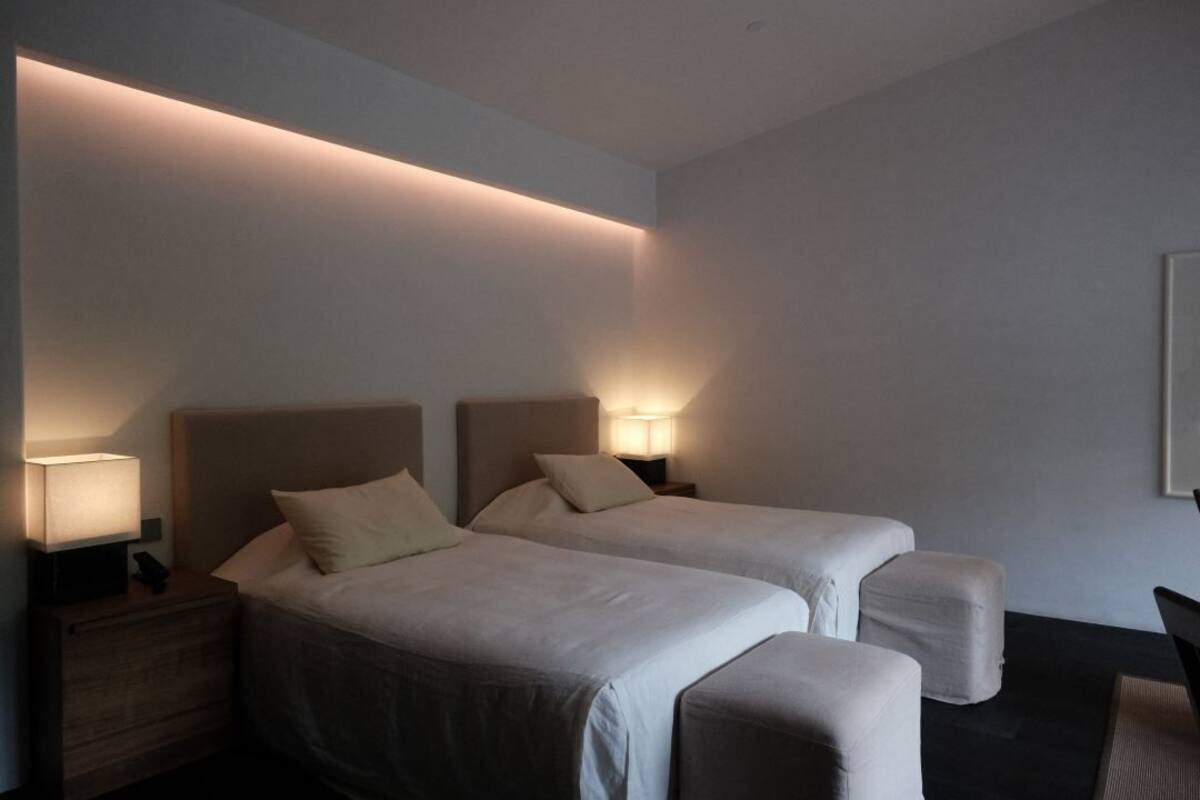 A modern hotel room with two beds, bedside lamps, a small table, and a chair.