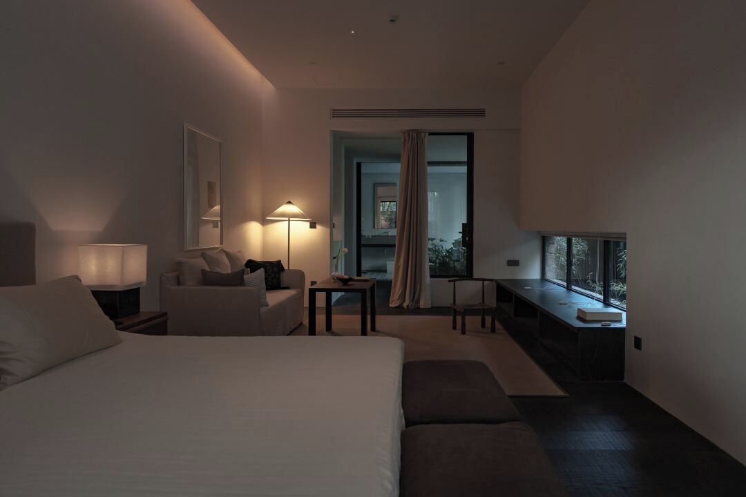A modern hotel room with a large bed, a desk, a chair, and a view of the outdoors.