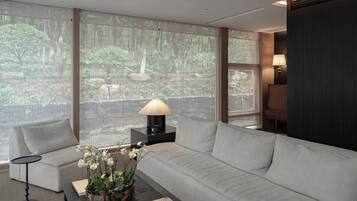 A modern living room with a large window, a sofa, a coffee table with a lamp, and a view of a forest.