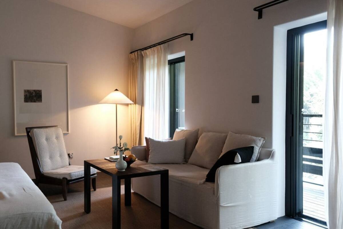 A hotel room with a bed, a sofa, a chair, a table with a lamp, and a window with curtains.
