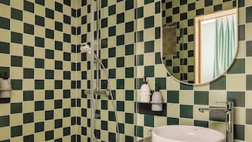 A bathroom with a checkered green and white tile wall, a shower with a handheld showerhead, a round sink with a marble countertop, and a mirror with a round frame.