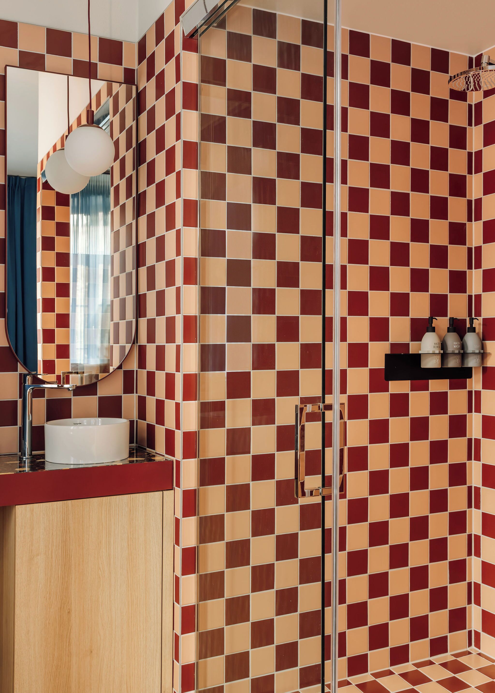 A bathroom with a checkered tile wall, a round sink, a mirror, and a shower area.