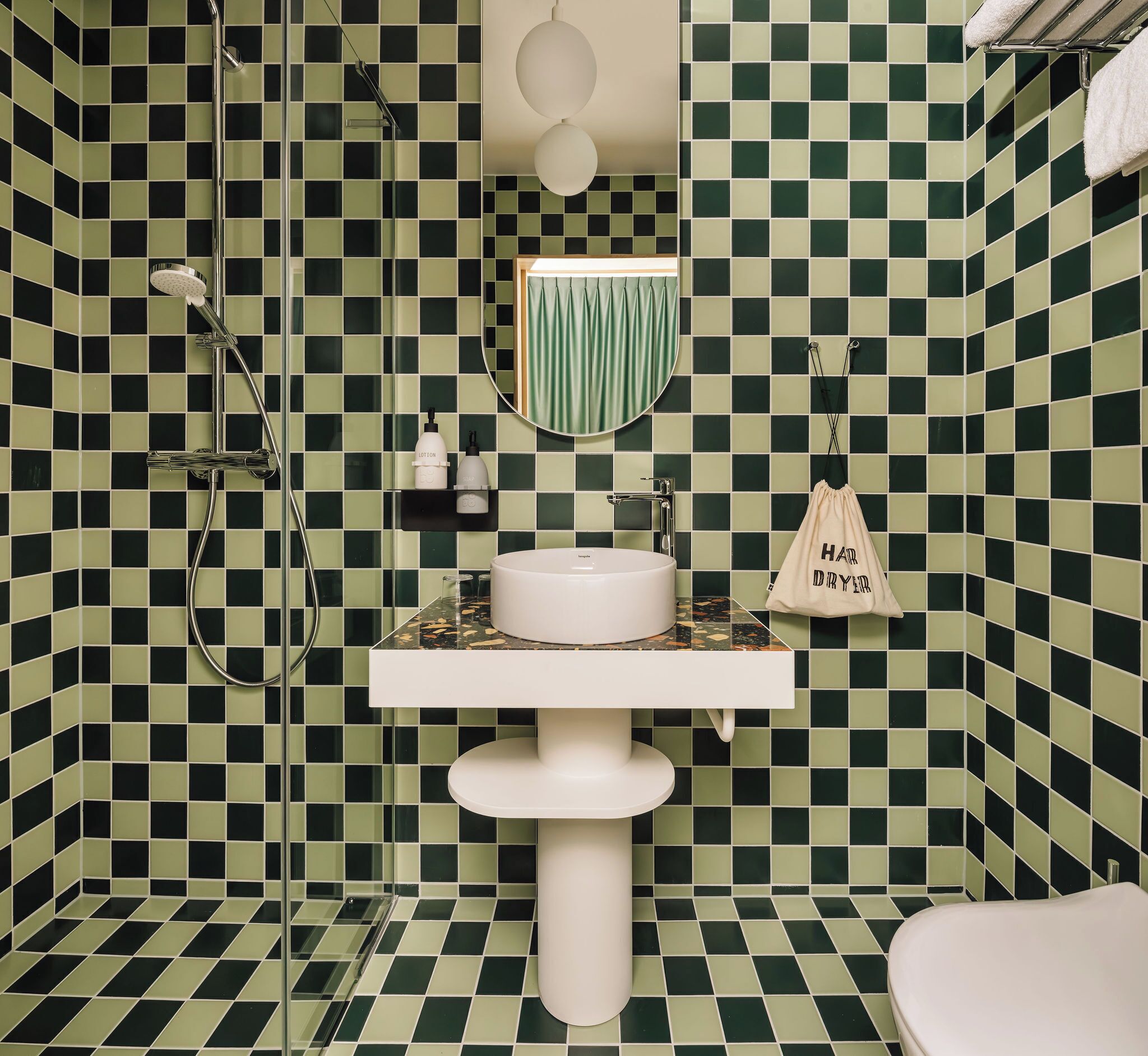 Een badkamer met een zwart-groen geruit tegelpatroon, een witte wastafel en een handdoek aan de muur.