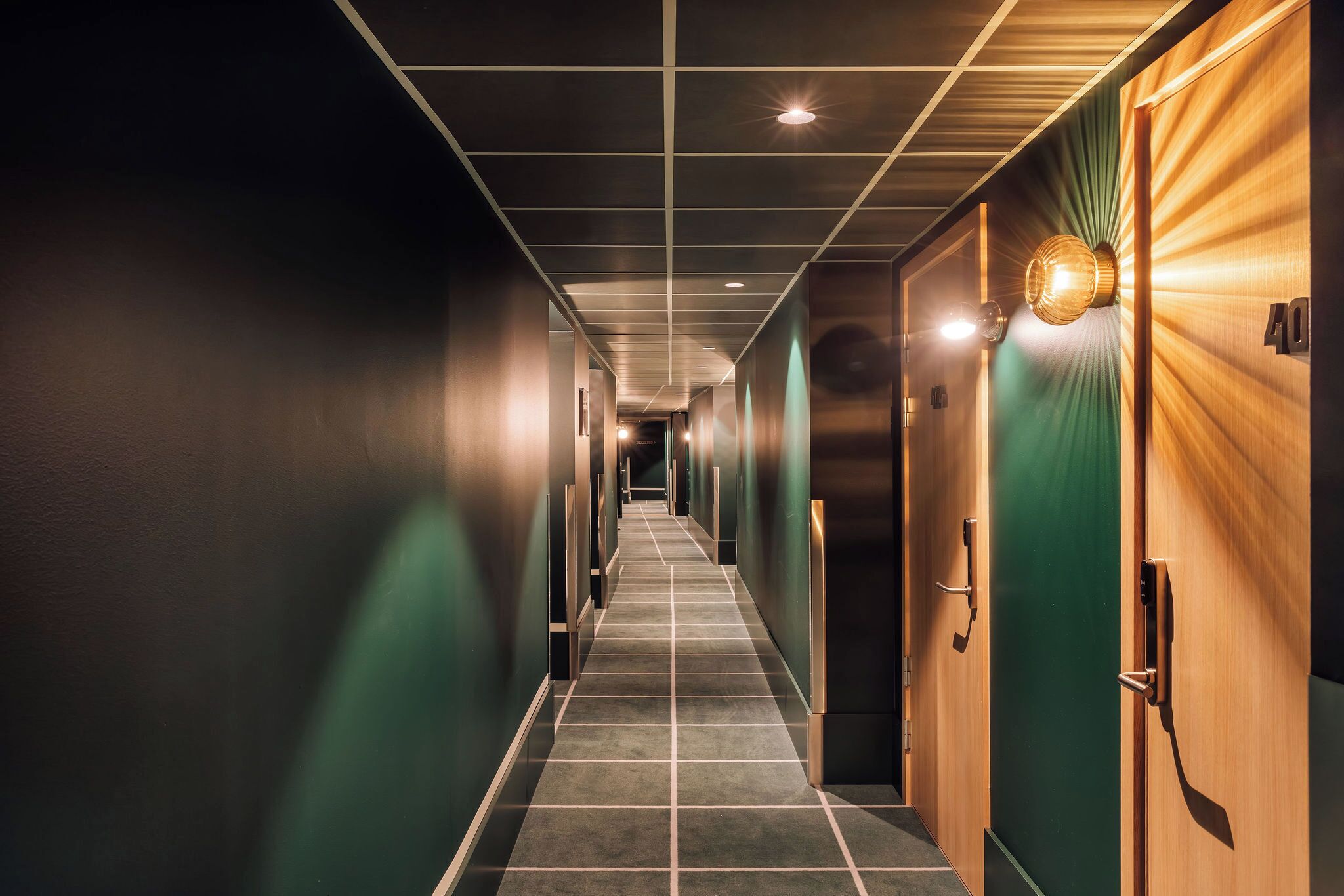 Un couloir doté d’un sol carrelé, de portes en bois et d’un mur d’accent de couleur verte.