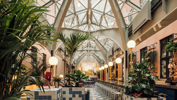 A spacious atrium with a high glass ceiling, featuring a checkered floor, seating areas, and a bar with a view of the city. - Hobo Oslo (Oslo)