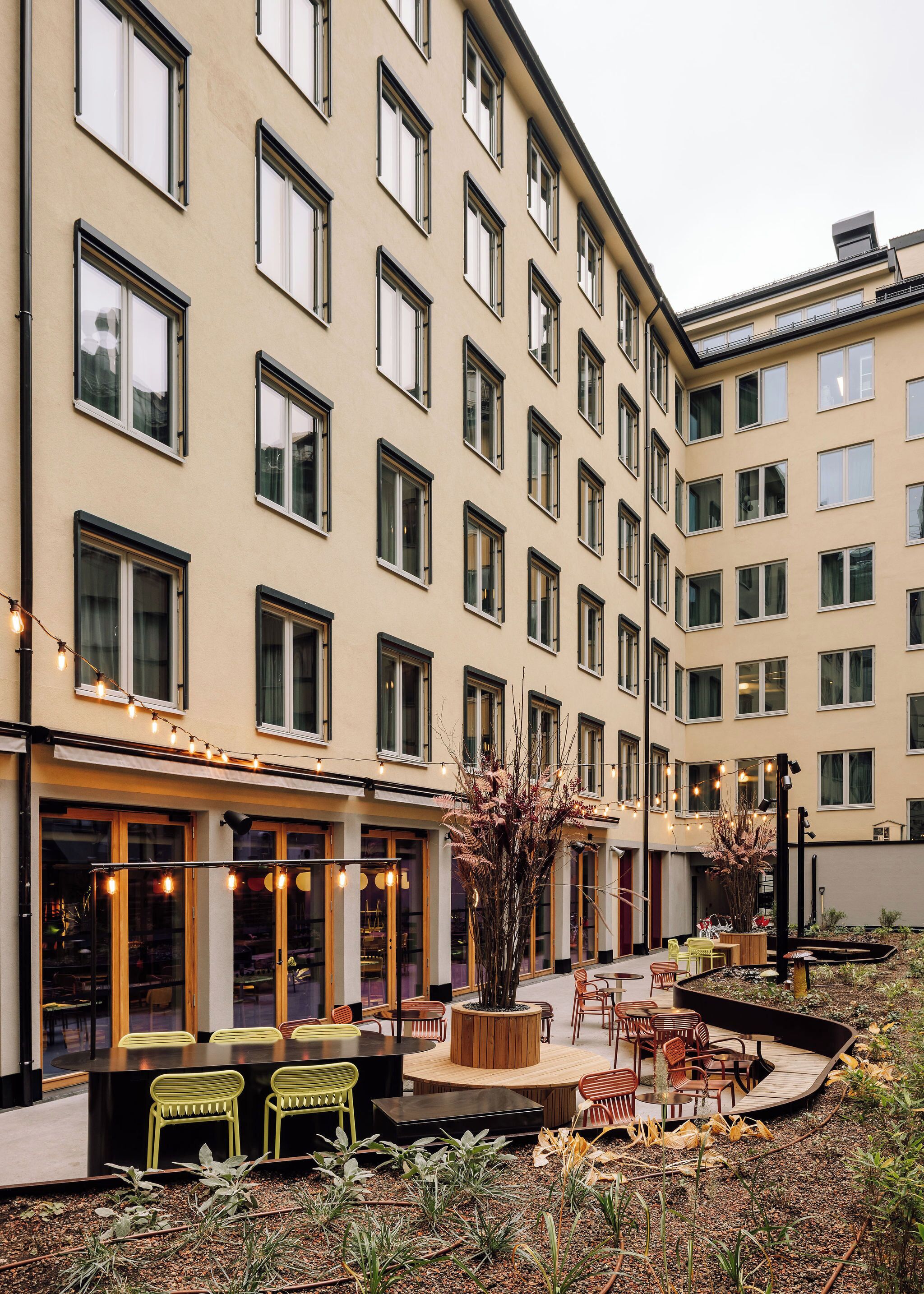 A hotel courtyard with outdoor seating, a small garden, and a building facade with multiple windows.