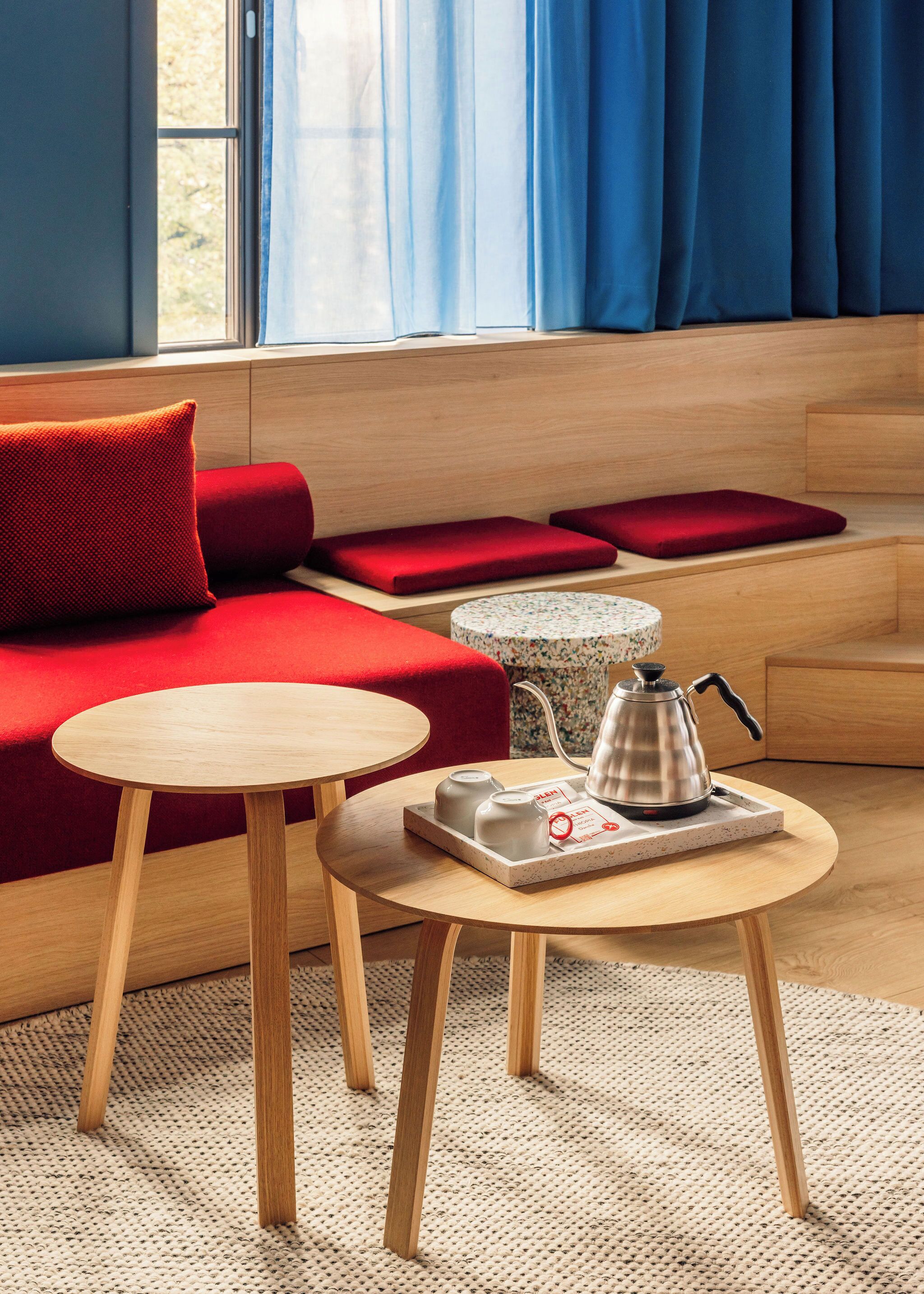 A cozy seating area with a red sofa, two wooden tables, and a coffee station.