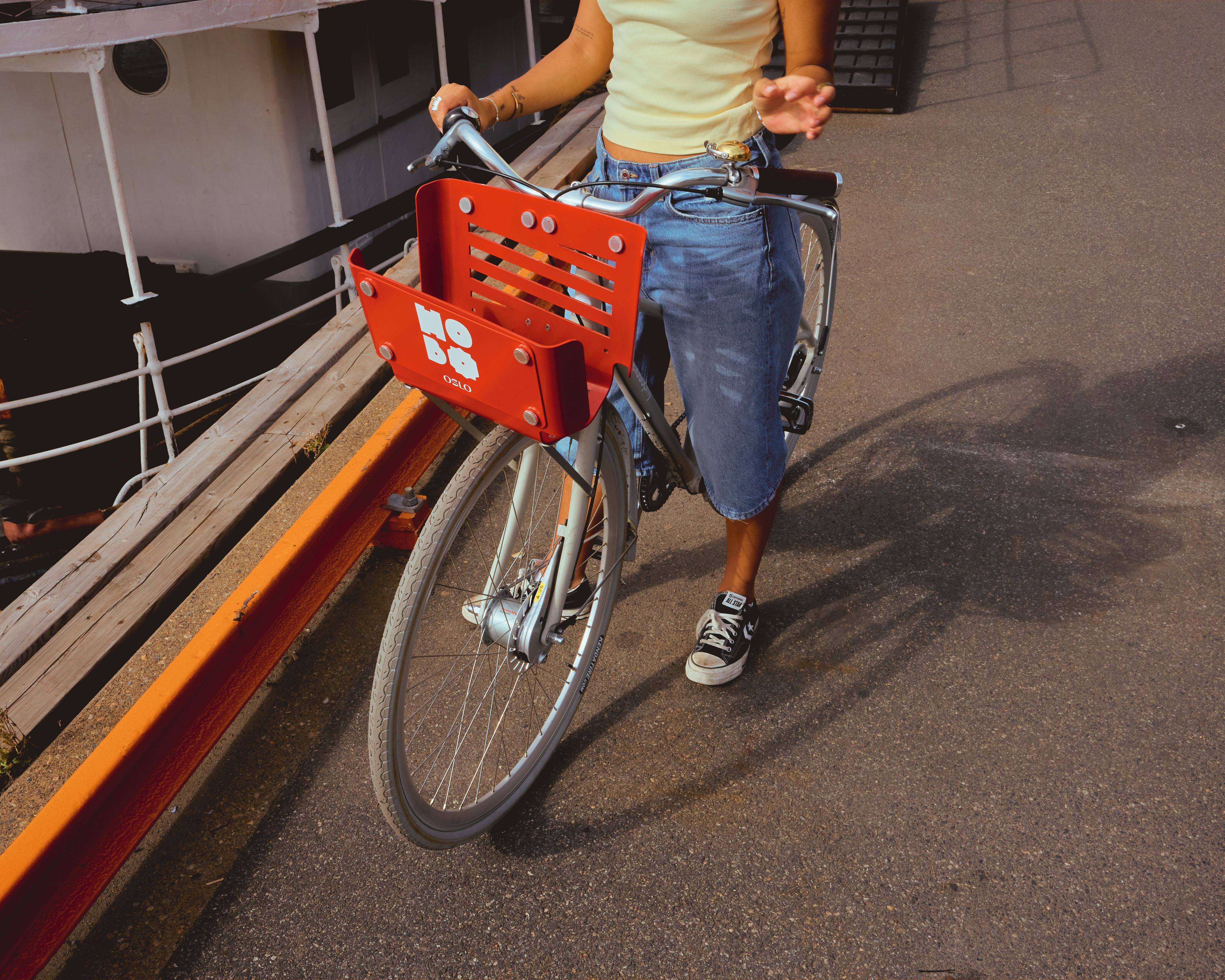 A person riding a bicycle with a red basket, wearing jeans and sneakers.