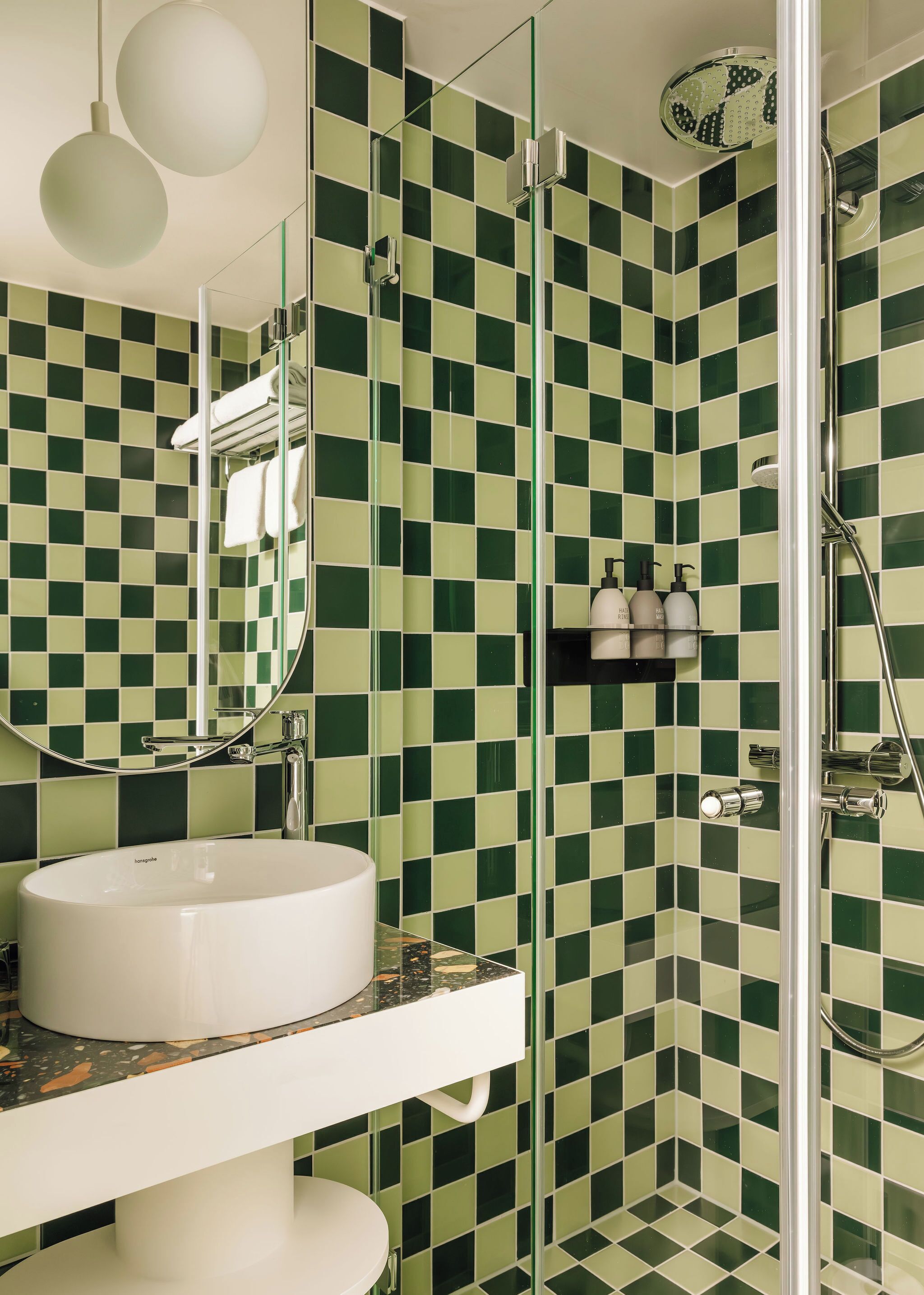 A bathroom with a checkered green and white tile wall, a white sink, and a glass-enclosed shower area.