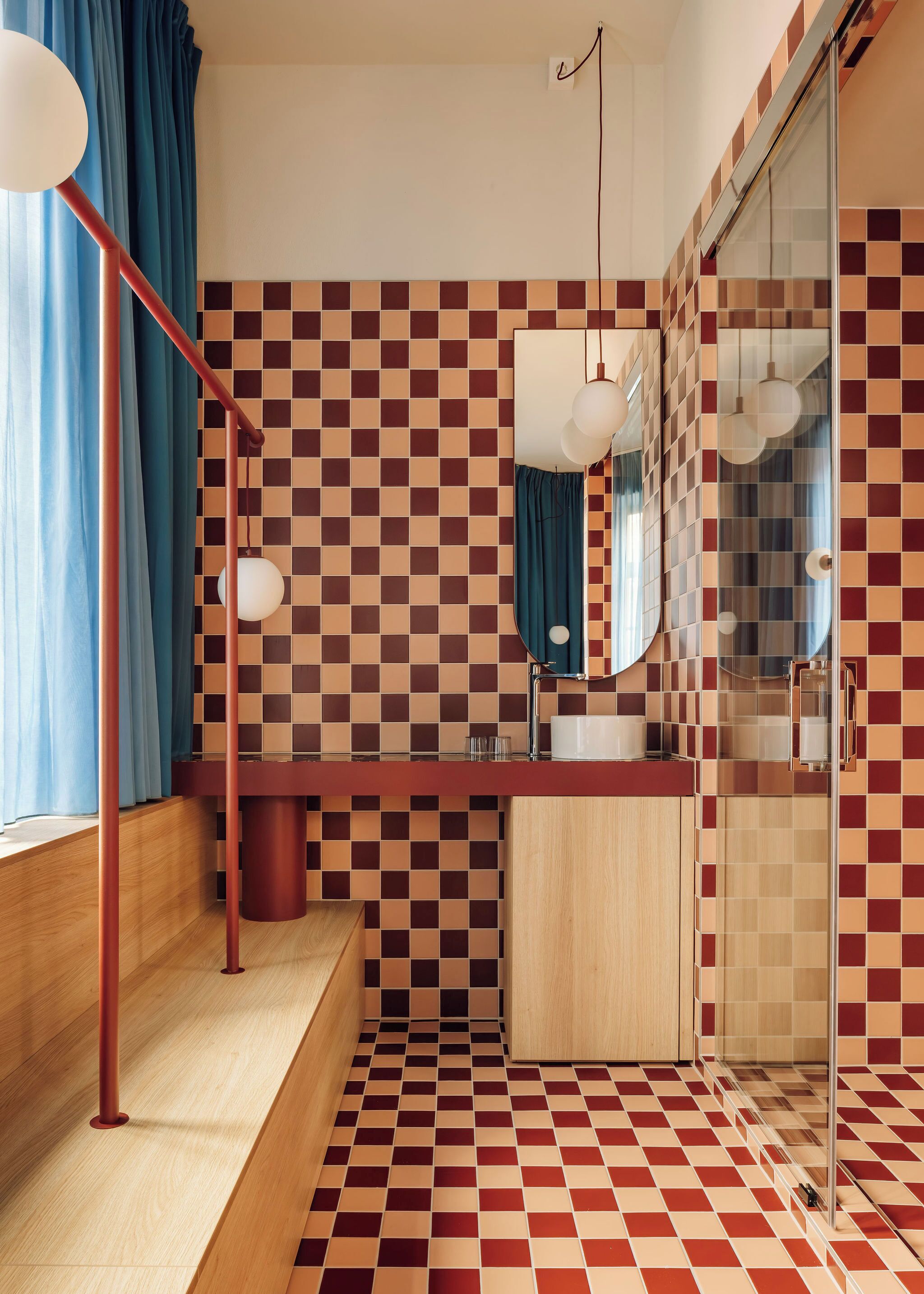 A bathroom with a checkered floor, a wooden vanity, a mirror, and a shower area.