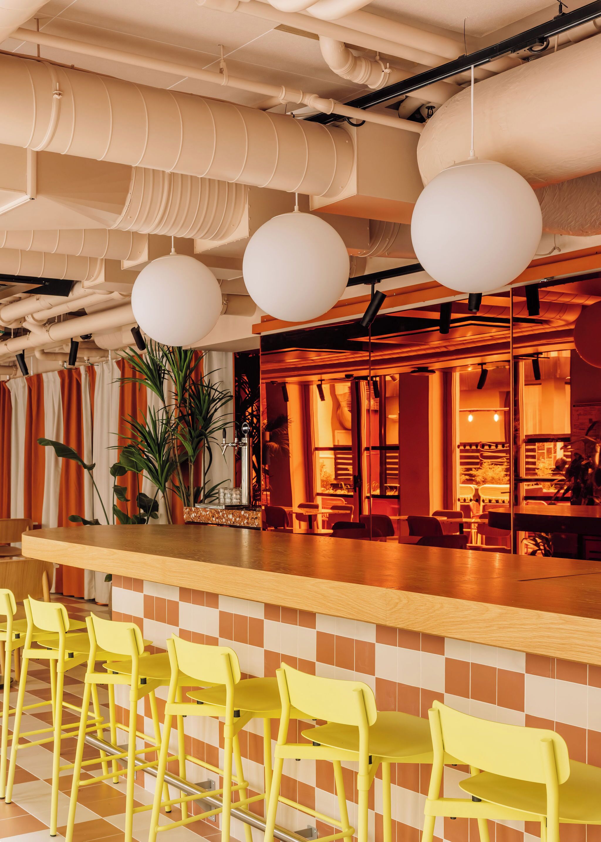 A bar area with yellow chairs, a wooden counter, and a warm interior with orange and white tiles.