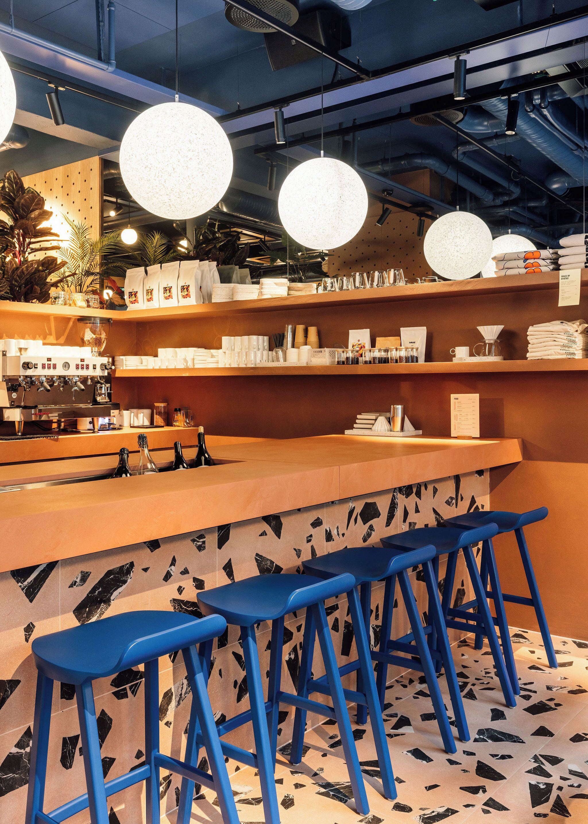Een bar met een counter, blauwe krukken en planken met diverse spullen.