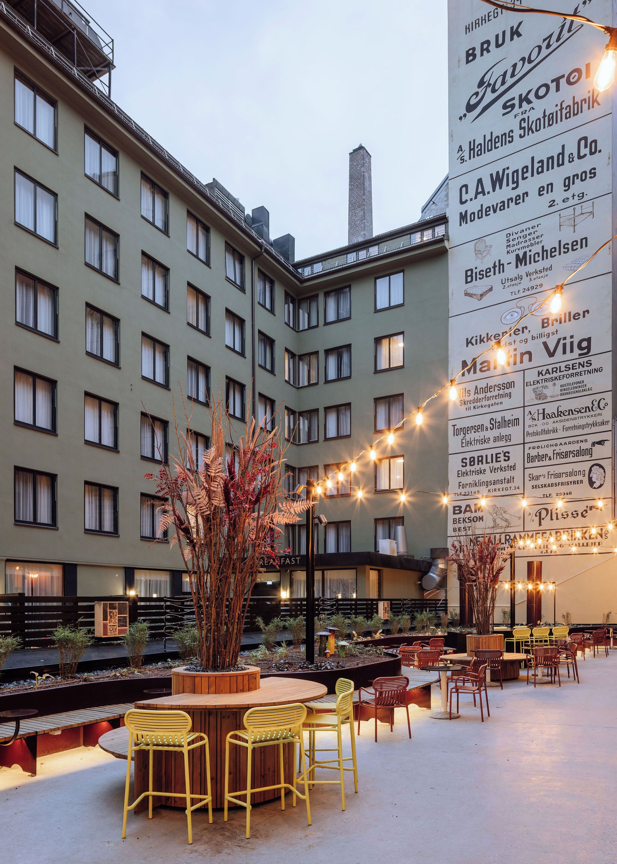 Un patio de hotel con mobiliario exterior y un edificio grande con numerosas ventanas y anuncios.