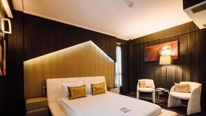 Une chambre d’hôtel avec un grand lit, deux fauteuils, une petite table et un téléviseur fixé au mur.