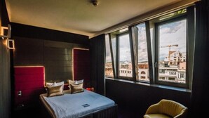 Une chambre d’hôtel avec un lit, une chaise et une grande fenêtre donnant sur la ville.