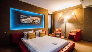 Une chambre d’hôtel moderne avec un grand lit, des fauteuils rouges, une œuvre d’art accrochée au mur et une lampe sur pied.