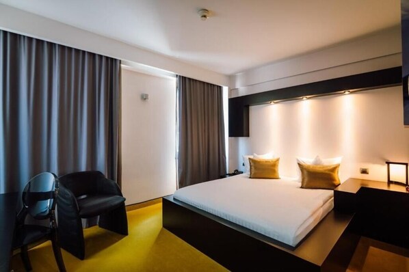 Une chambre d’hôtel avec un lit, deux oreillers, une chaise, un bureau et un téléviseur.