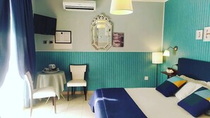 A hotel room with a bed, a small table, a chair, a wall-mounted air conditioner, and a decorative mirror. - La Contessa B&B (Mercogliano)