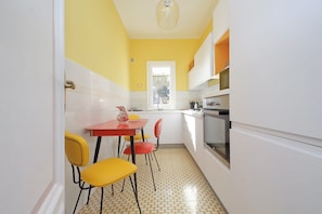 A kitchen with a yellow wall, white cabinets, a red table, and yellow chairs. - 4bnb - Monteverde Chic Comfort (Rome)