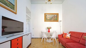 A living room with a TV, red and white furniture, a painting, and a vase with flowers. - 4bnb - Monteverde Chic Comfort (Rome)