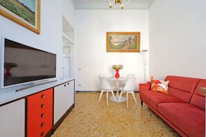 Un salón con televisor, muebles rojo y blanco, un cuadro y un jarrón con flores.