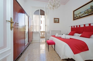 A hotel room with a bed, a red blanket, a white pillow, a red bench, a chandelier, and a painting on the wall. - 4bnb - Monteverde Chic Comfort (Rome)