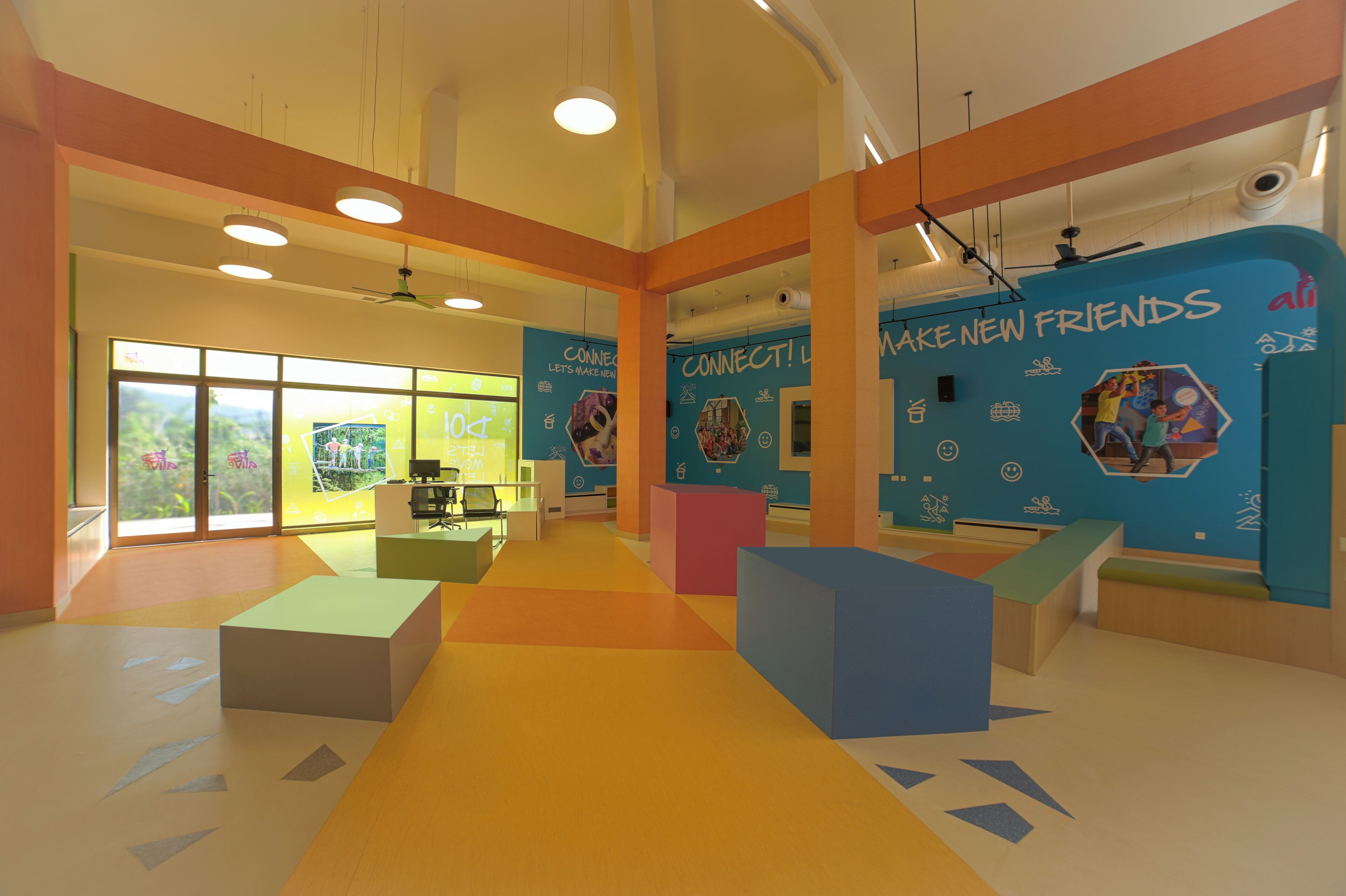 Un espacio interior luminoso con paredes coloridas, ventanas amplias y diferentes zonas de estar.