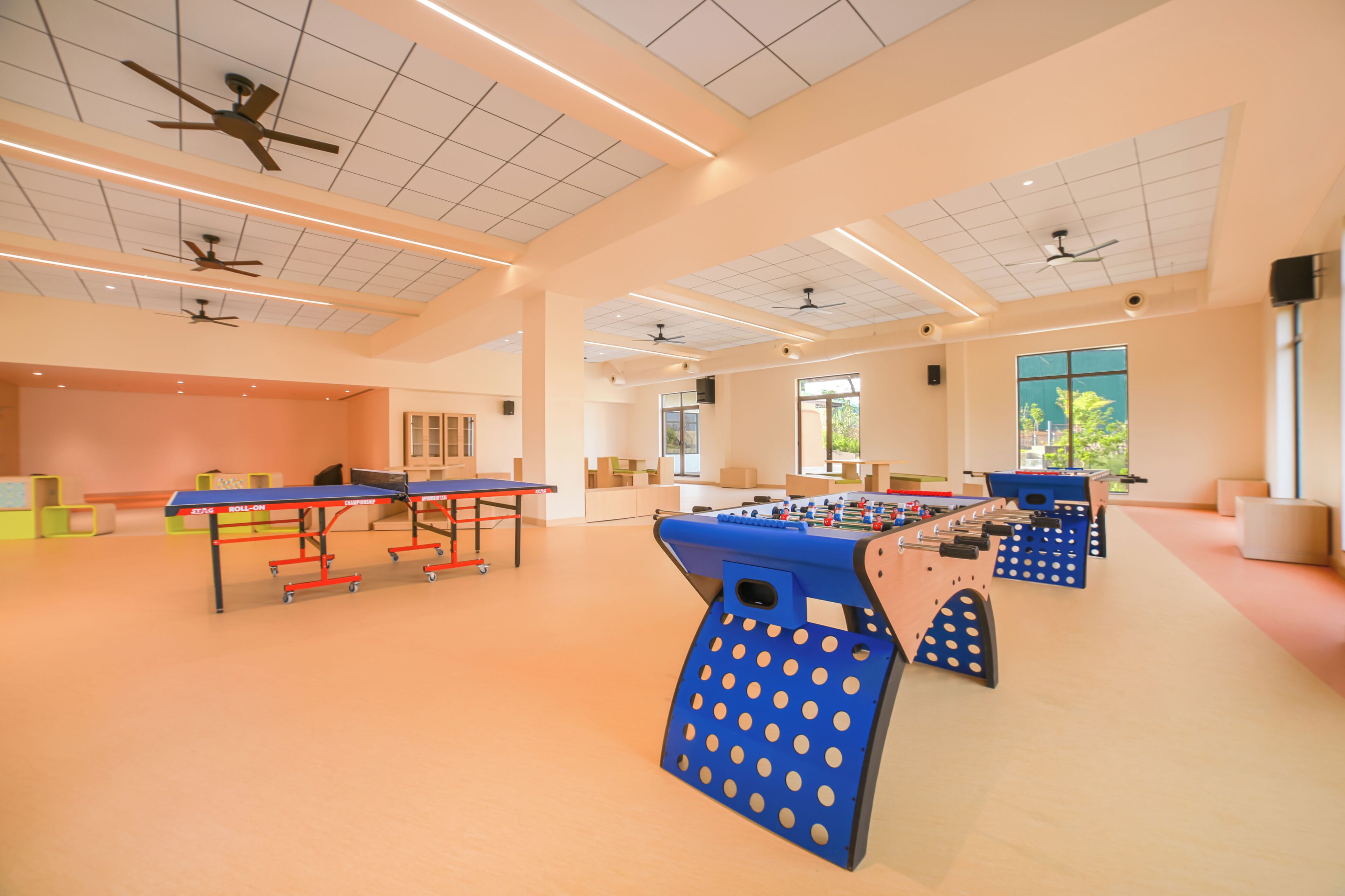 A spacious indoor area with ceiling fans, a foosball table, and a ping pong table.