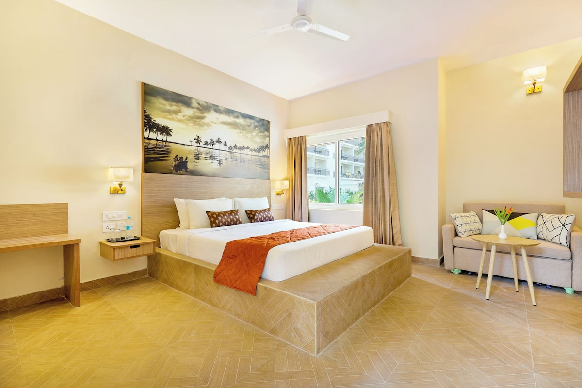 A hotel room with a bed, bedside table, lamp, and a painting on the wall.