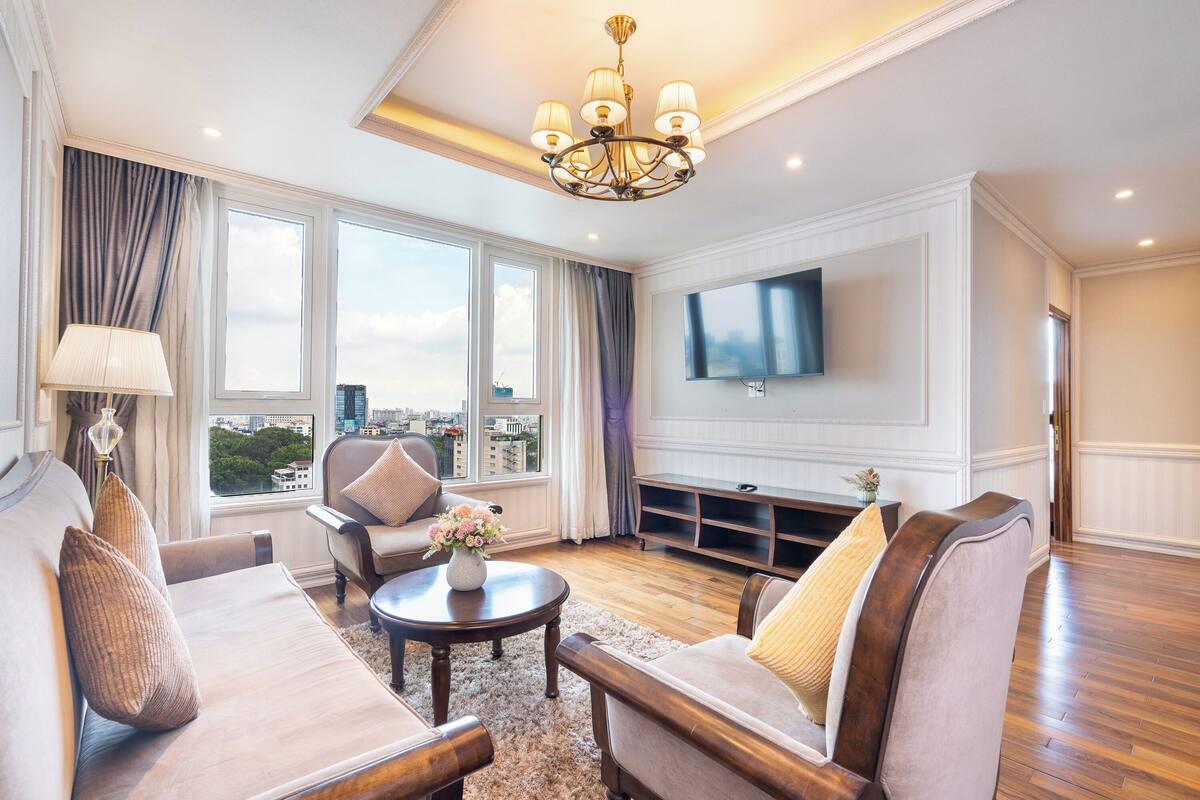 Ein geräumiges Wohnzimmer mit großem Fenster, einer Chandelüster und einem an der Wand befestigten Flachbildfernseher.