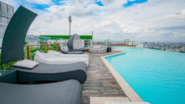 Una piscina infinita en la azotea con sillas de descanso y vista a la ciudad.