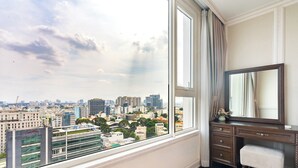 Una habitación con un ventanal amplio que ofrece vistas a la ciudad, un escritorio de madera con cajones y un espejo.