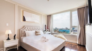 Habitación de hotel con una cama grande, una mesita de noche con lámpara, televisión y vista a la ciudad.