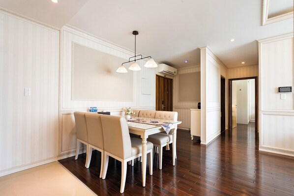 Un comedor con mesa y sillas blancas, una lámpara colgante y suelo de madera.