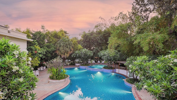 A swimming pool surrounded by lush greenery and a building. - Club Mahindra Golden Landmark (Mysore)