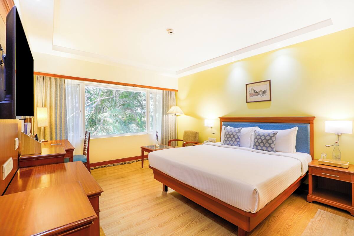 A hotel room with a large bed, wooden furniture, a desk, and a window with curtains.