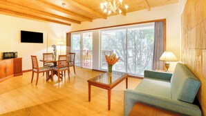 A spacious living room with wooden flooring, a glass coffee table, a sofa, and a dining area with chairs and a table. - Club Mahindra Golden Landmark (Mysore)