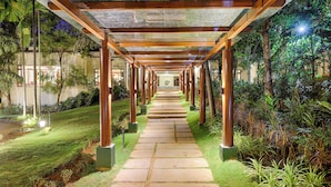 A pathway with a wooden pergola structure, surrounded by lush greenery and a well-maintained lawn. - Club Mahindra Golden Landmark (Mysore)