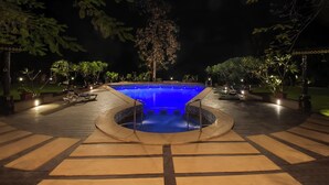 A swimming pool with a circular hot tub in the center, surrounded by a deck with seating and potted plants. - Club Mahindra Netrang (Netrang)