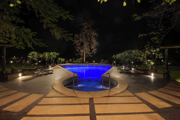 A swimming pool with a circular hot tub in the center, surrounded by a deck with seating and potted plants.