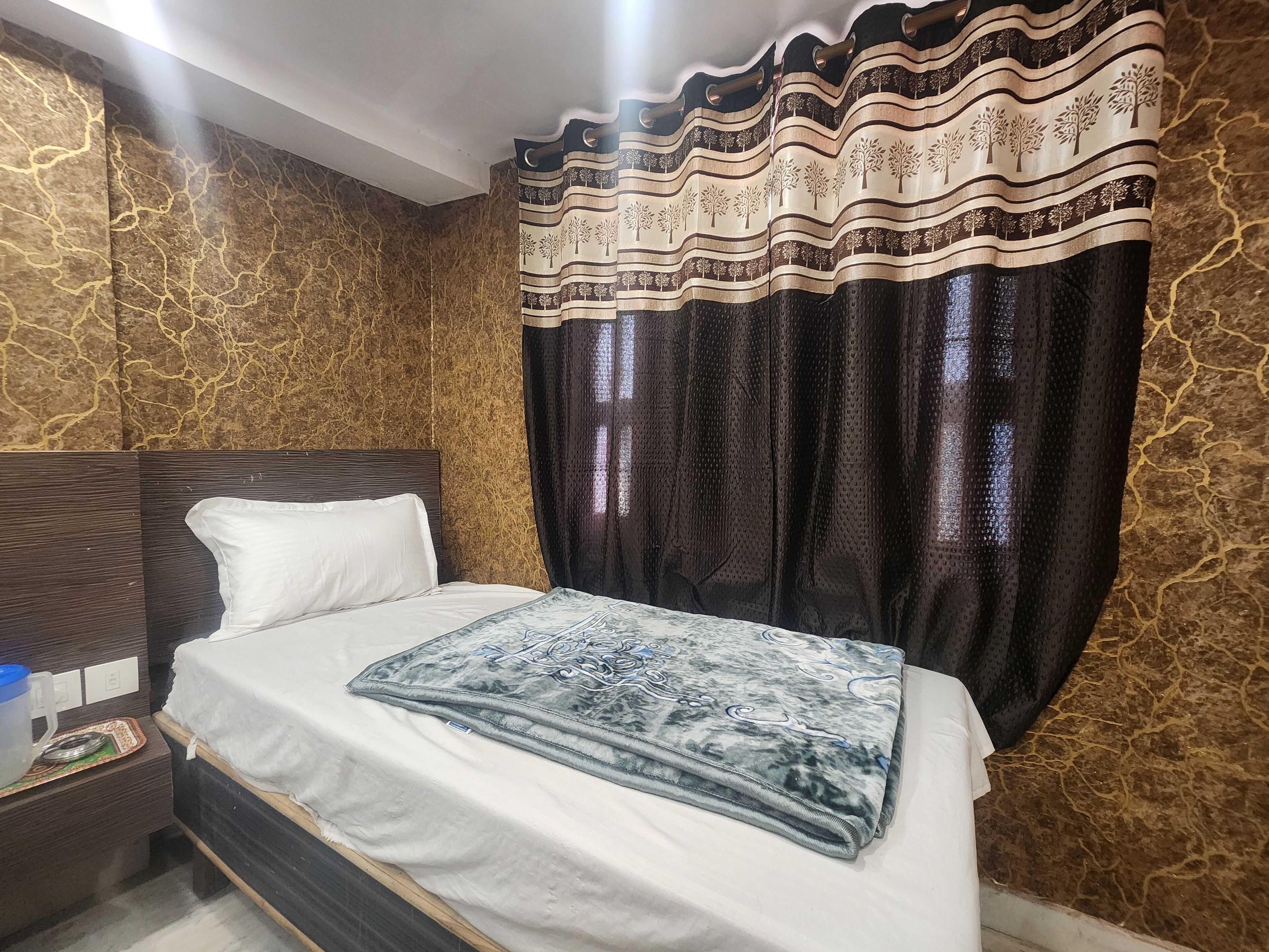 A hotel room with a bed, a nightstand, and a curtain with a tree pattern.